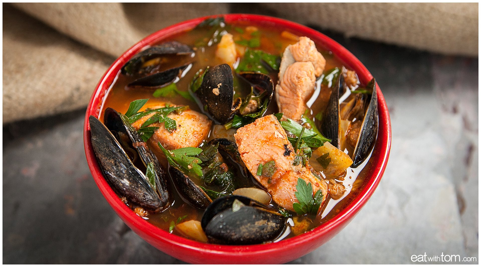Seafood stew recipe in red bowl with mussels salmon and cilantro - tom schmidt photographer